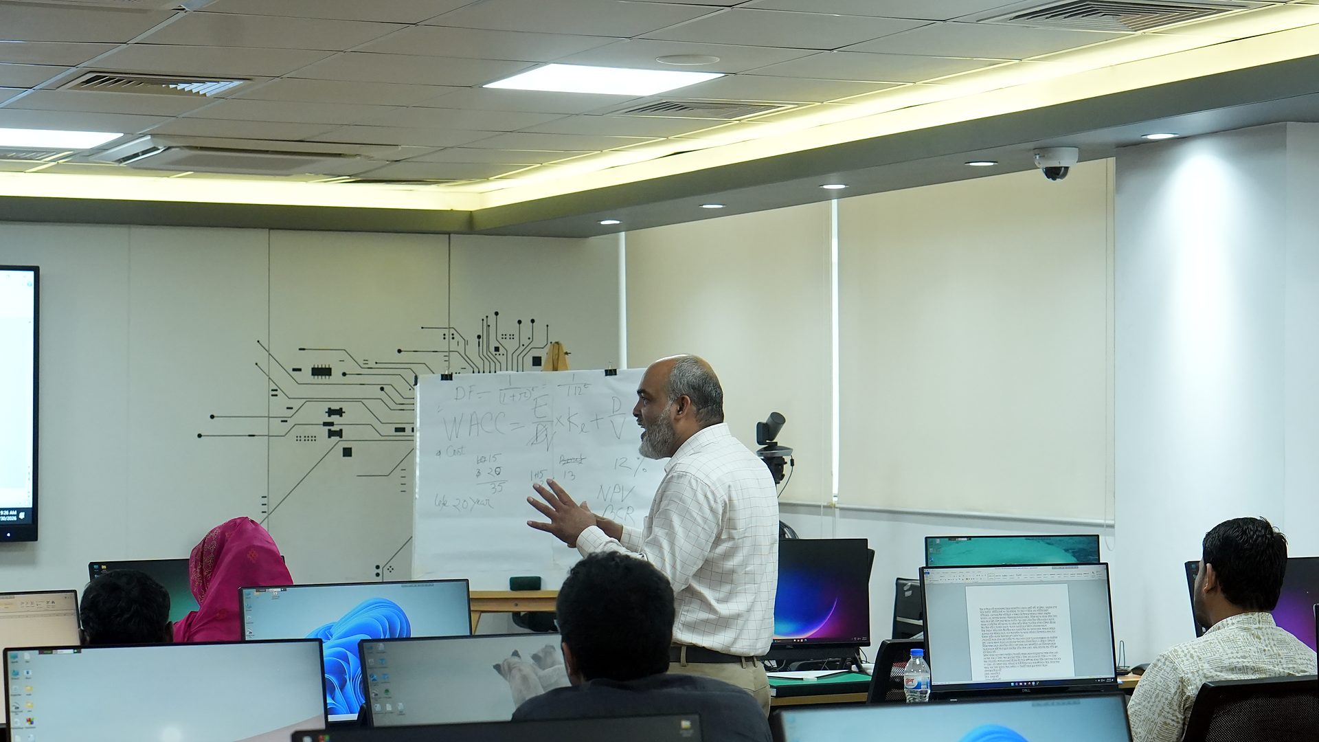 Resource person explaining an economic analysis concept at the whiteboard