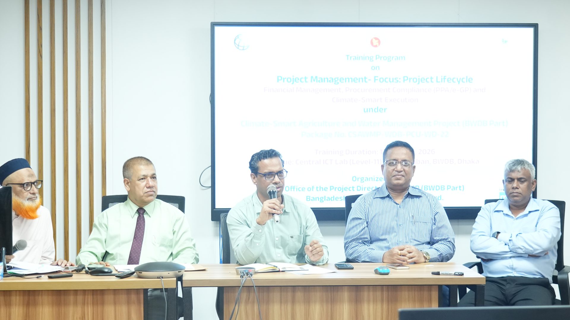 The Project Director addressing the closing ceremony from the head table, with the training programme banner displayed on screen