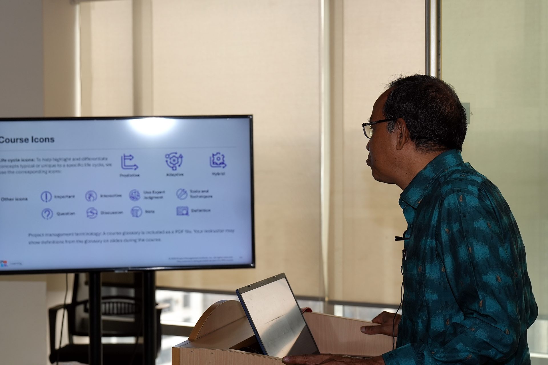 Trainer at the lectern beside the Course Icons slide showing predictive, adaptive and hybrid life-cycle icons