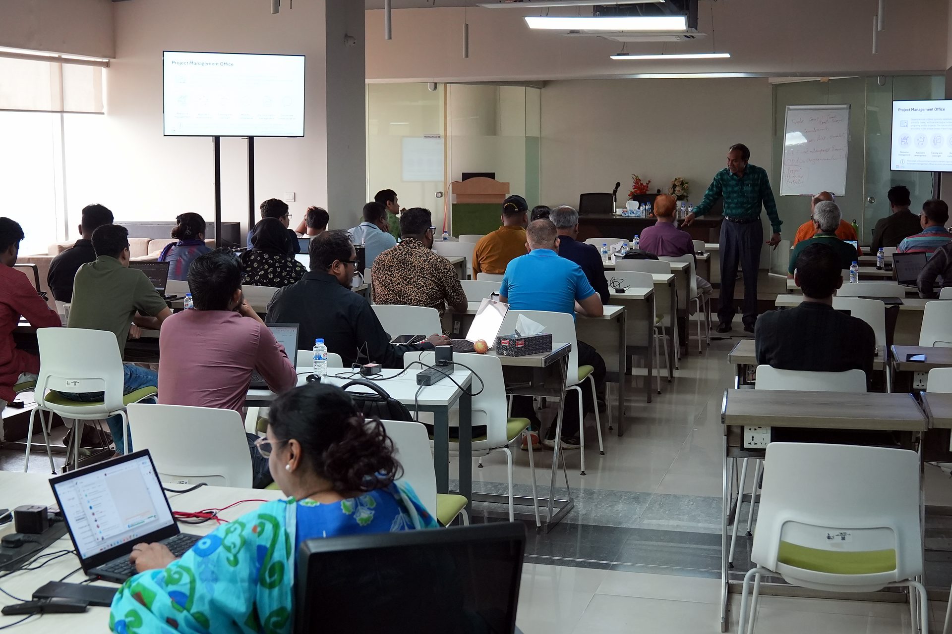 Wide view of PMP Day 3 with the cohort at their laptops and the trainer at the front of the a2i training room